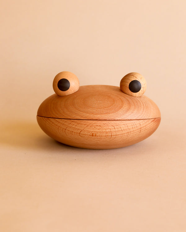 A Spring Copenhagen The Frog Bowl, resembling a frog made of beechwood, with a smooth, round body and two prominent, spherical eyes attached on top, against a plain beige background.
