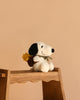 The Plush Peanuts Snoopy with Woodstock in Backpack, featuring black ears and a brown backpack, sits on a wooden step stool against a plain beige background.