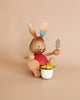 A Collectible Dregeno Easter Figure - Rabbit Gardener With Flower Pot, made in Germany, with a red shirt, holding a trowel and sitting in a white pot filled with colorful flowers. It has a blue flower behind one ear.