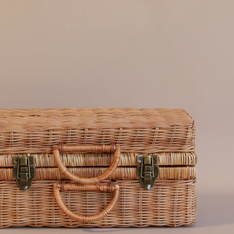 A natural Rattan Toaty Trunk with a closed lid, featuring two front clasps and a handle, set against a light pink background.