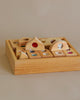 Bauspiel Fairytale Mixed Gemstone Set With Tray (36 pieces) sensory play set with various shapes containing colorful translucent insets, neatly arranged in a square wooden tray on a beige background. This Bauspiel wooden toy enhances cognitive development through tactile exploration.
