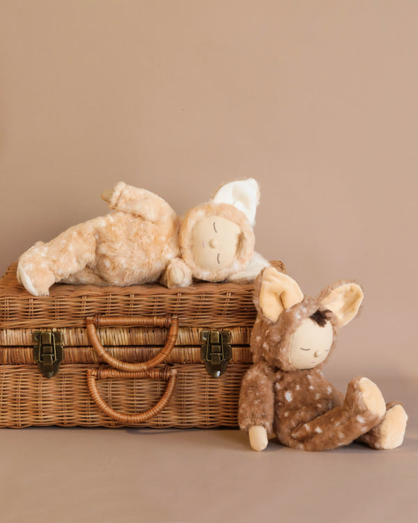 Two stuffed dolls in deer costumes photographed against a rattan suitcase. 