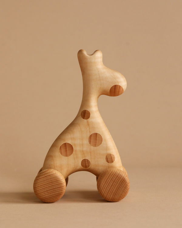 A **Handmade Wooden Mini Giraffe Push Toy** with a minimalist design. It has a smooth, light brown finish with darker brown spots, and four circular wooden wheels at the bottom, allowing it to roll. This delightful kids' giraffe push toy sits against a soft beige background that complements the natural wood tones.