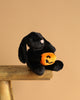 The Steiff Mr. Spice Hoppie Rabbit, a black bunny with floppy ears, sits on a wooden bench holding an orange jack-o'-lantern plush against a plain beige background.