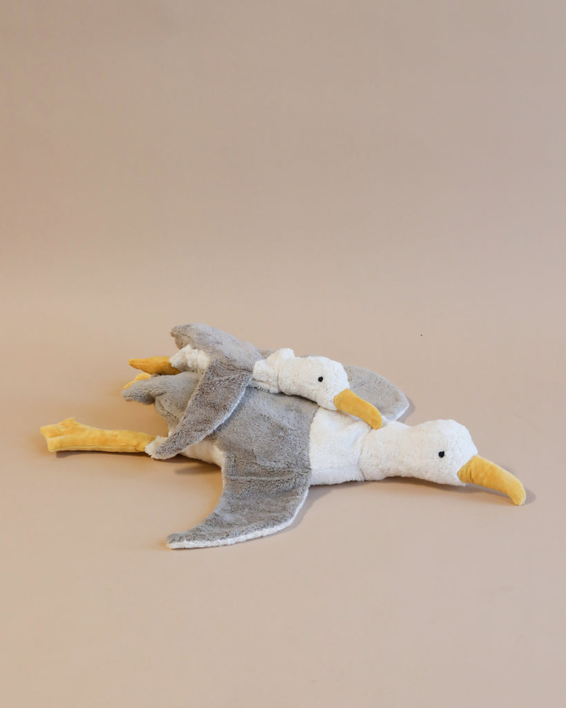 Two Senger Naturwelt Cuddly Animal Seagull toys filled with organically grown cotton, lying side by side on a plain beige background, with one overlapping the other slightly, both facing to the right.