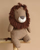 A PRE-ORDER Maileg Safari Friends Big Lion toy, shipping in February, with a shaggy brown mane and a soft, handmade body sits on a wooden bench against a neutral beige background.