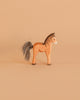 The Ostheimer Brown Colt is a handcrafted wooden horse figurine with a painted mane and tail of dark fibers, standing on a light brown surface—ideal for imaginative play.