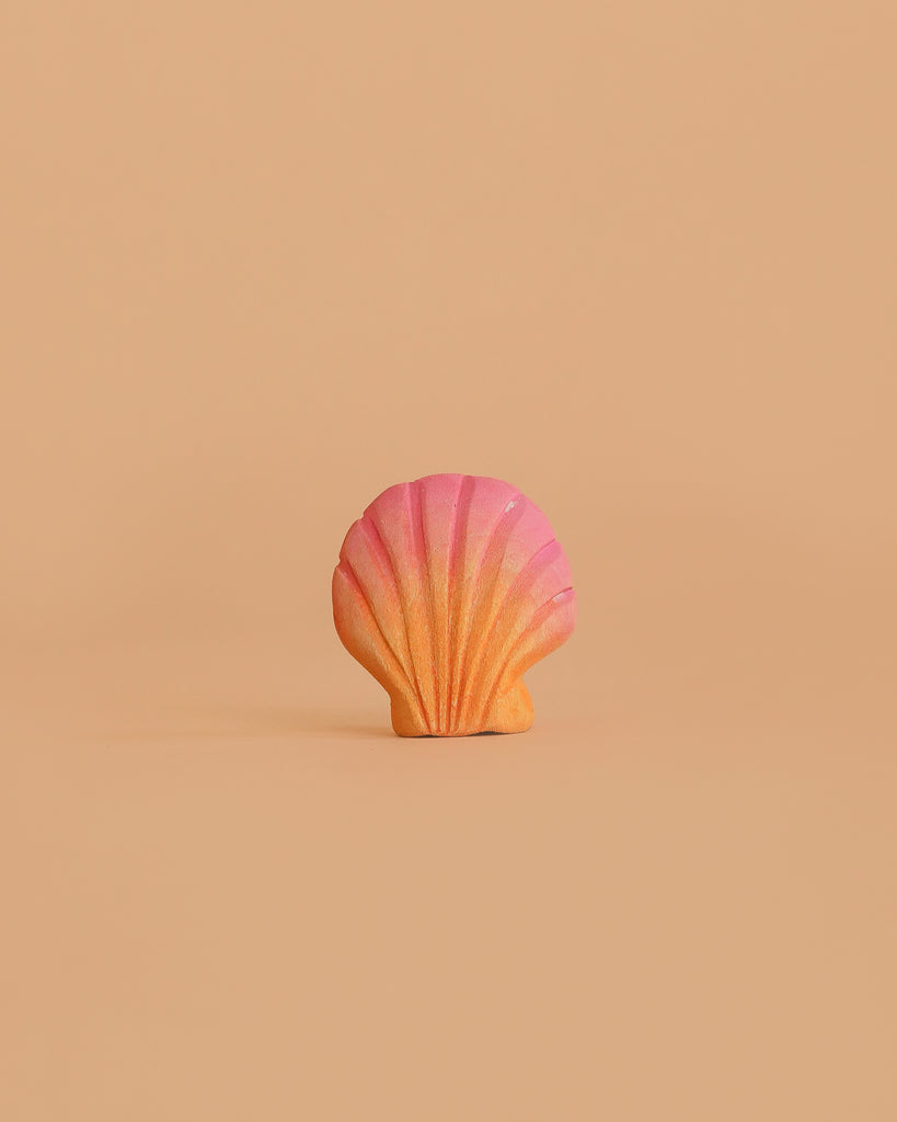 A pink and orange seashell-shaped object is centered against a plain, light beige background, echoing the style of the Bumbu Handmade Wooden Ocean Set.