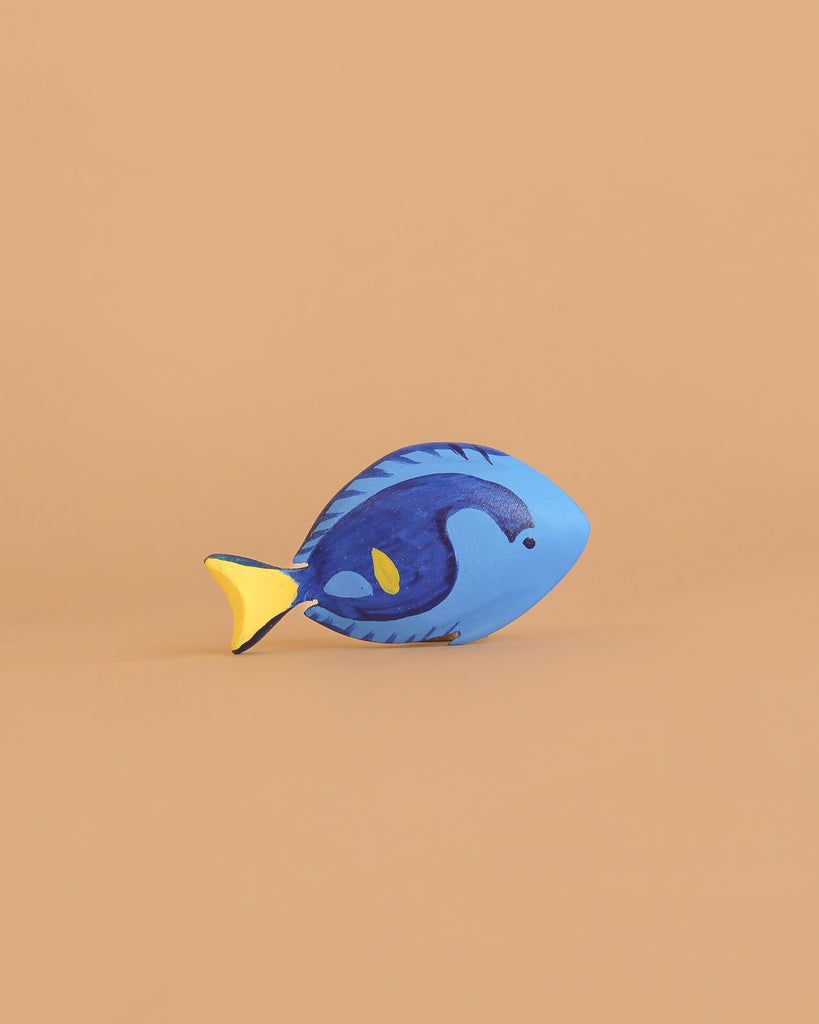 The Bumbu Handmade Wooden Royal Blue Fish, featuring blue and yellow painted details, is a sustainable Montessori toy displayed on a plain light brown background—perfect for mindful play.