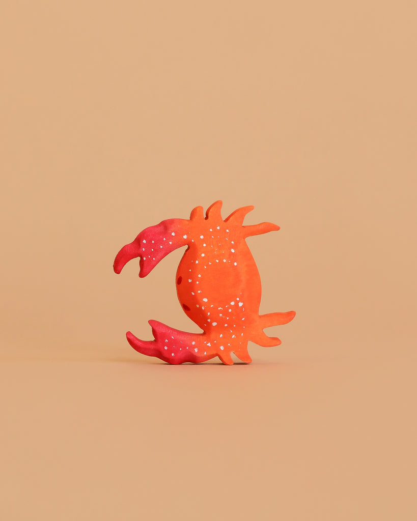 The Bumbu Handmade Wooden Red Crab features bright orange-red hues, white dots, and stylized curved claws. Crafted from sustainable wood, it stands upright on a beige background—ideal for Montessori-inspired play or decorative display.
