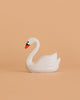 A small, white figurine from the Bumbu Handmade Wooden Swan Set with an orange beak is shown against a plain peach background.