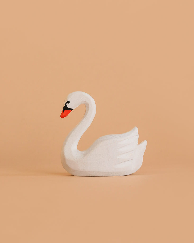 The Bumbu Handmade Wooden Swan, a small handcrafted toy with an orange beak, is displayed against a plain peach-colored background.