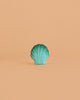 A turquoise seashell stands upright against a plain peach background, capturing the charm of the Bumbu Handmade Wooden Ocean Set.