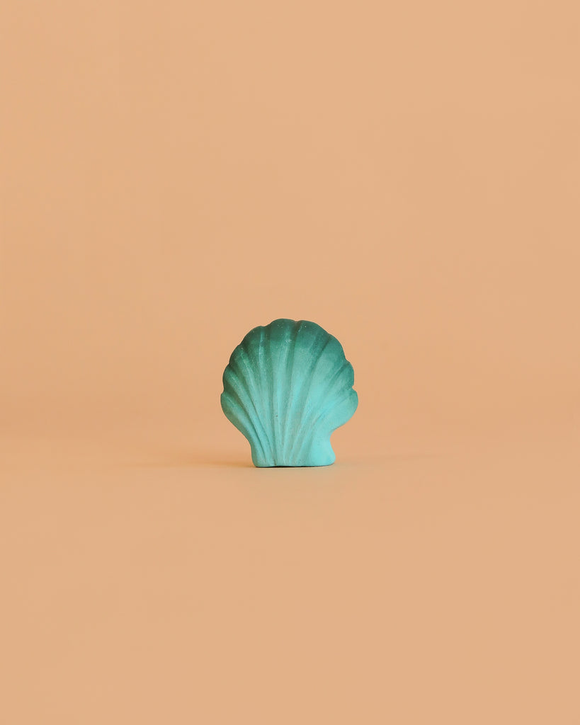 A handmade Bumbu Wooden Green Seashell is centered on a simple peach background, highlighting its Montessori-inspired design.