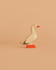The Bumbu Handmade Wooden Domestic Duck is a small, handcrafted toy featuring a beige body, orange beak, and orange feet, displayed on a solid light peach background.