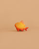 The Bumbu Handmade Wooden Golden Fish, featuring orange and yellow hues with red fins, is displayed against a simple, light brown background.