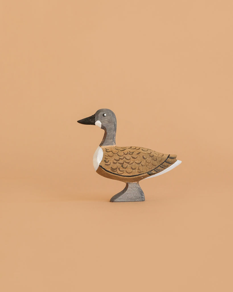 The Bumbu Handmade Wooden Wild Goose is a small, handcrafted wooden toy painted in brown, gray, black, and white and stands on a plain light tan background.