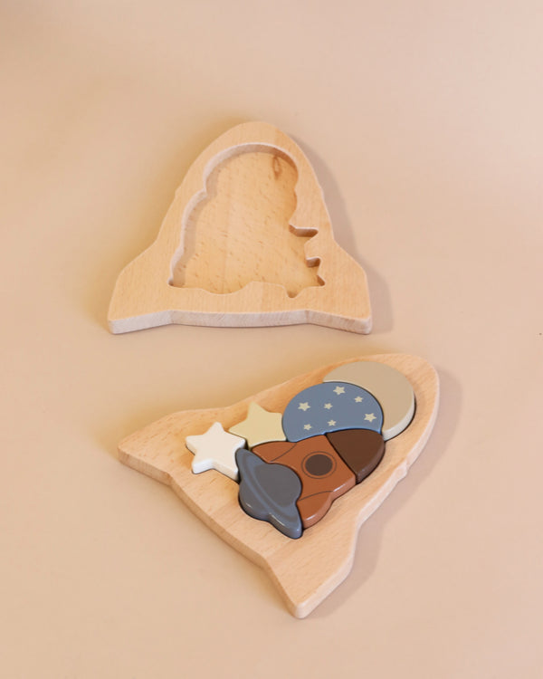 A wooden puzzle crafted from FSC-certified wood in the shape of a rocket with three pegged pieces designed like an ice cream scoop with a star and a hat, arranged against a soft