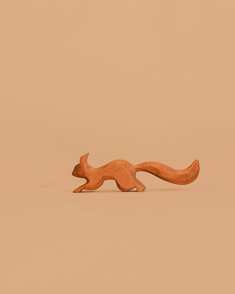 The Bumbu Handmade Wooden Squirrel Running, featuring a large bushy tail, sits against a plain light brown background, inspiring imaginative forest adventures.