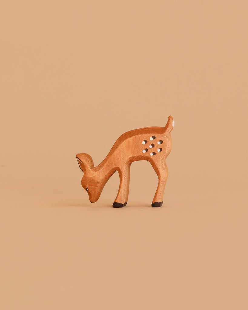 The Bumbu Handmade Wooden Fawn Eating is a small, brown wooden toy with white spots, depicted grazing with its head lowered—an eco-friendly choice ideal for imaginative play.