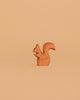 A small squirrel from the Bumbu Handmade Wooden Woodland Animals Set stands upright on a plain, light brown background, its tail curved upward and body facing left.