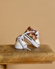 A pair of small, leopard-print baby sneakers with white laces, perfect for the Minikane Standing Doll (14") - Zoelie With Outfit & Shoes, sits on a rustic wooden surface against a beige background.