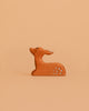 The Bumbu Handmade Wooden Fawn Resting features a small, handcrafted brown design with white spots. Its minimalistic look and eco-friendly wood make it a charming toy or decor piece for any space. The fawn gazes upward as it rests.