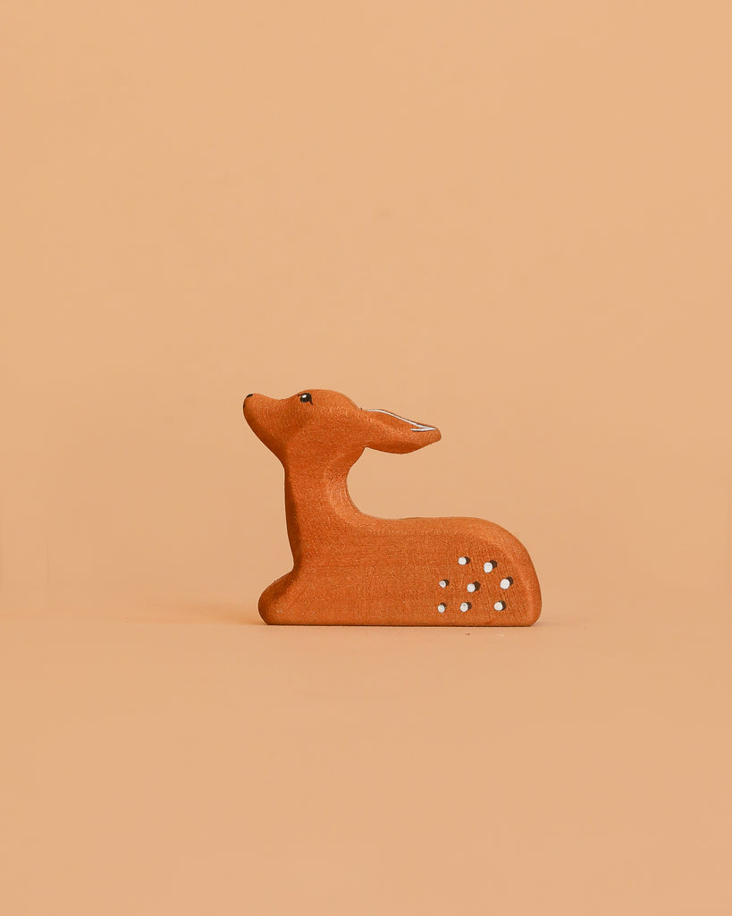 The Bumbu Handmade Wooden Fawn Resting features a small, handcrafted brown design with white spots. Its minimalistic look and eco-friendly wood make it a charming toy or decor piece for any space. The fawn gazes upward as it rests.