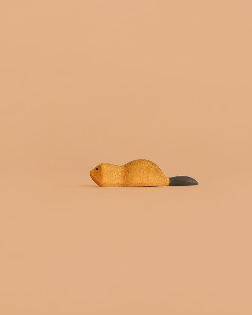 The Bumbu Handmade Wooden Baby Beaver features a minimalist light brown body and dark tail, set against a beige background—an ideal eco-friendly toy perfect for Montessori playrooms.