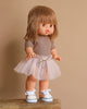 A Minikane Standing Doll (14") - Zoelie in a pink tutu stands on a wooden surface, wearing a brown top and white sneakers with brown accents against a beige background, exuding a natural vanilla scent.