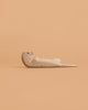 The Bumbu Handmade Wooden Otter Sleeping figure rests on its back against a peach backdrop, bringing eco-friendly charm and unique decor to any room.