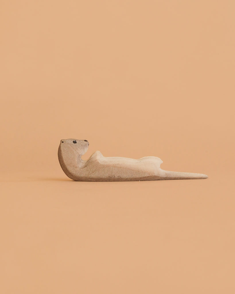 The Bumbu Handmade Wooden Otter Sleeping figure rests on its back against a peach backdrop, bringing eco-friendly charm and unique decor to any room.