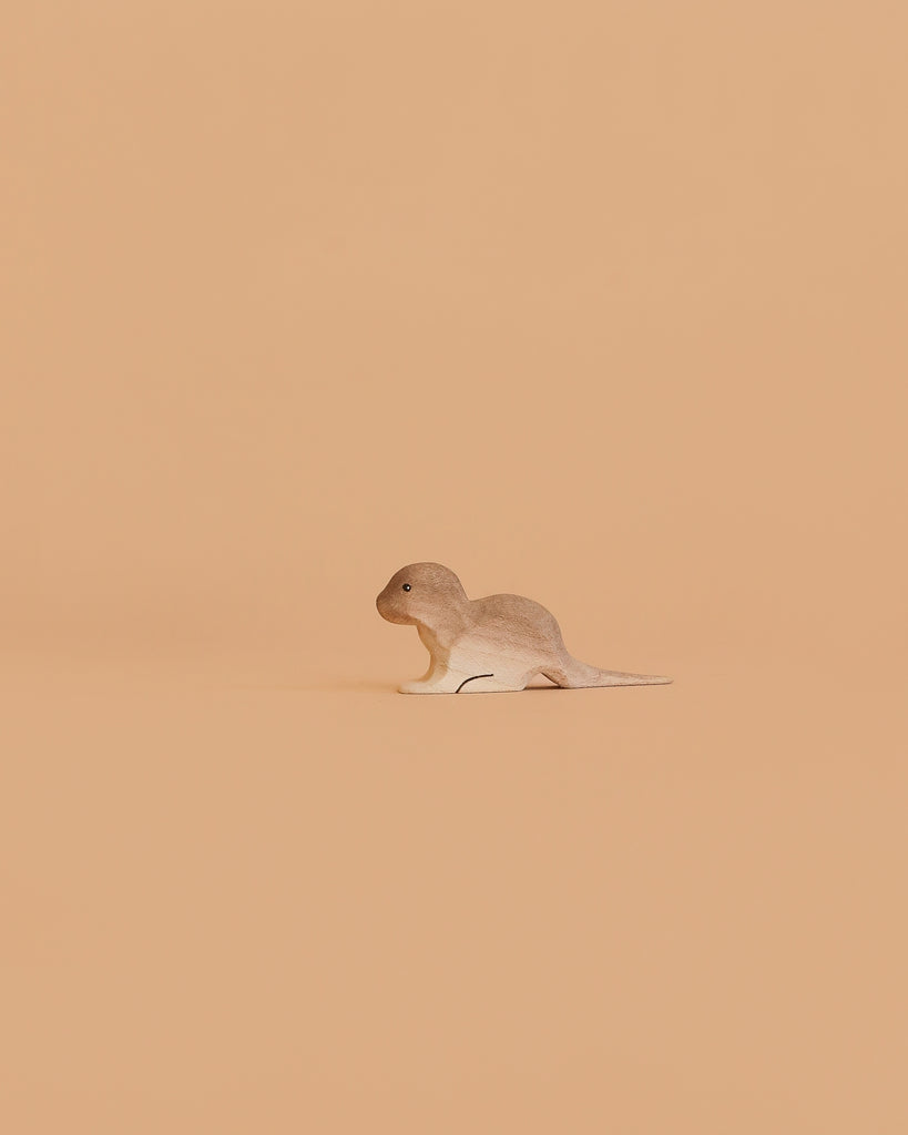 The Bumbu Handmade Wooden Baby Otter toy stands slightly left on a plain, peach-colored background.