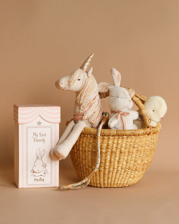 A Easter Basket Set filled with stuffed animals, including a Maileg unicorn and a bunny, next to a box titled "my first bunny" against a soft beige background.