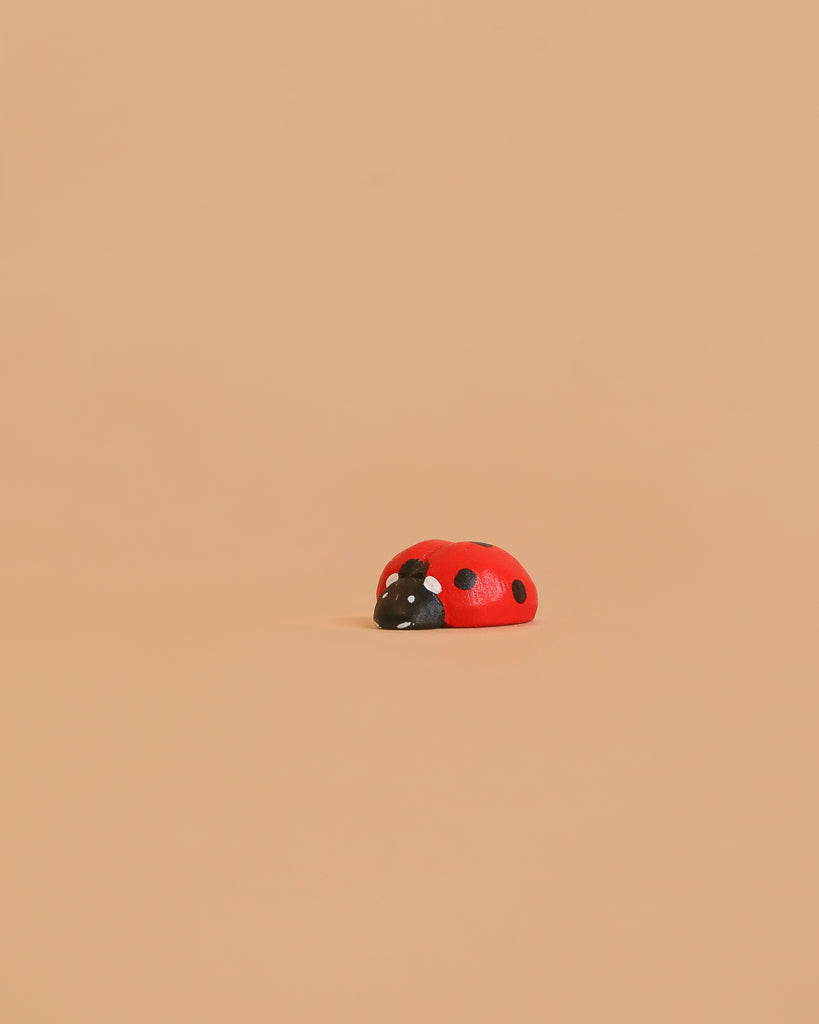 The Bumbu Handmade Wooden Ladybug, a small red wooden toy with black spots, rests on a plain light beige background.