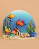 The Bumbu Handmade Wooden Ocean Set, featuring crab and turtle figures, is displayed in an underwater scene with a blue background, sandy foreground, and peach backdrop alongside colorful clay sea creatures.