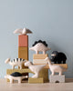A collection of hand-painted wooden animal figurines, including a bird, Handmade Tiny Wooden Dinosaurs - T-Rex, and various mammals, artfully arranged on and around stacked pastel-colored blocks against a light blue background.
