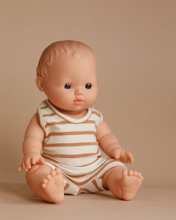 A Minikane Doll (13") - Louis with Marcel Set in Brown Sugar Stripes Outfit, featuring a bald head, sits against a plain beige background. Its phthalate-free vinyl limbs are slightly spread apart, inviting imaginative playtime as it gazes slightly to the side.