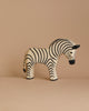 A handcrafted zebra figurine from the Ostheimer Handmade Wooden Safari Animals Set stands on a beige surface against a matching background, perfect for imaginative play and reminiscent of classic wooden toys.