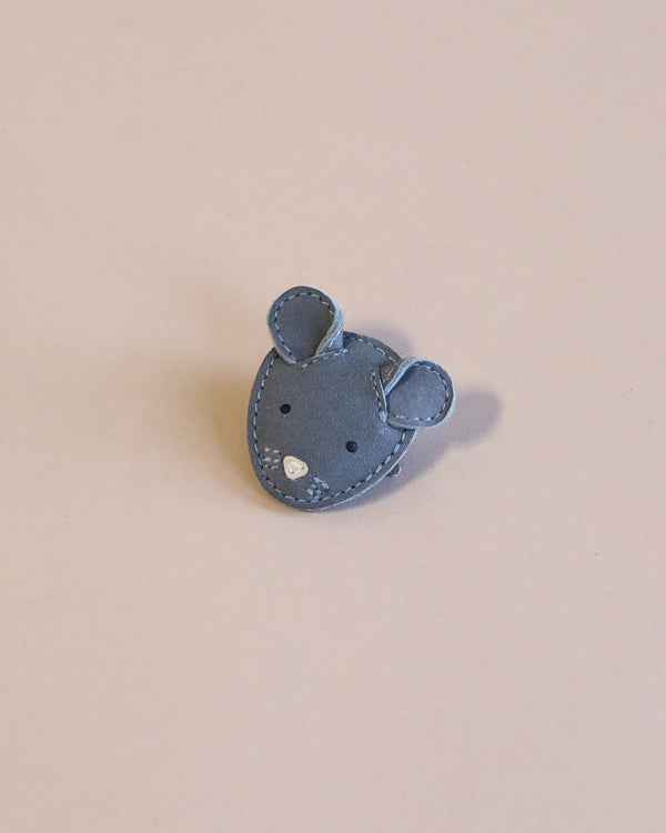A small gray mouse Donsje Leather Hairclip with intricate stitching and sparkling details, set against a soft pink background, is handmade with premium leather.