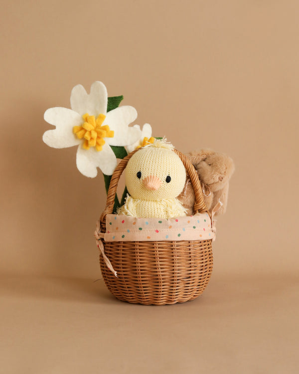 A Cuddle & Kind duckling and a Maileg mini bunny peek out from a Small Easter Basket Set adorned with a floral fabric. A white and yellow felt flower leans against the basket on a
