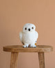 A Steiff x Harry Potter Set Hedwig owl plush with yellow eyes sits on a wooden stool against a plain beige background.