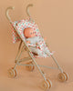 The Minikane Soft Body Doll (11") - Claire with Clothing and Stroller is displayed in a beige toy stroller with floral fabric, set against a peach-colored background.