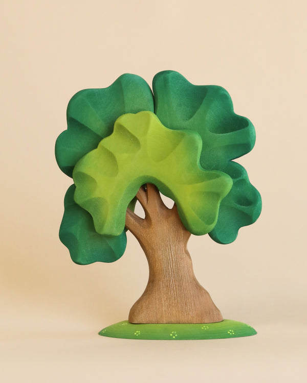 A whimsical sculpture of the Extra Large Wooden Tree crafted from linden wood with a vibrant green canopy and a brown trunk, set against a plain light beige background. The tree appears cartoonish with expressive features.