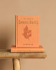 An orange hardcover Collector's Edition of "The Memoirs of Sherlock Holmes" by Arthur Conan Doyle stands upright on a horizontal book, set against a wooden surface with a beige background. The cover features an elegant illustration of oak leaves.