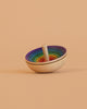 The Mader UFO Spinning Top - Purple Rainbow features vibrant concentric circles on a light peach background. Its simple wooden design and playful colors shine as it tilts, highlighting its unique charm.