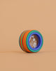 The Mader Wooden Compound Eye Lens, featuring a blue-rimmed magnifying glass and colorful maple wood rings, is displayed on a beige background.