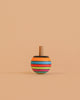 The Mader Turn-Over Top - Striped, made of maple wood with orange, blue, green, red, and black horizontal stripes, stands upright on a beige background.
