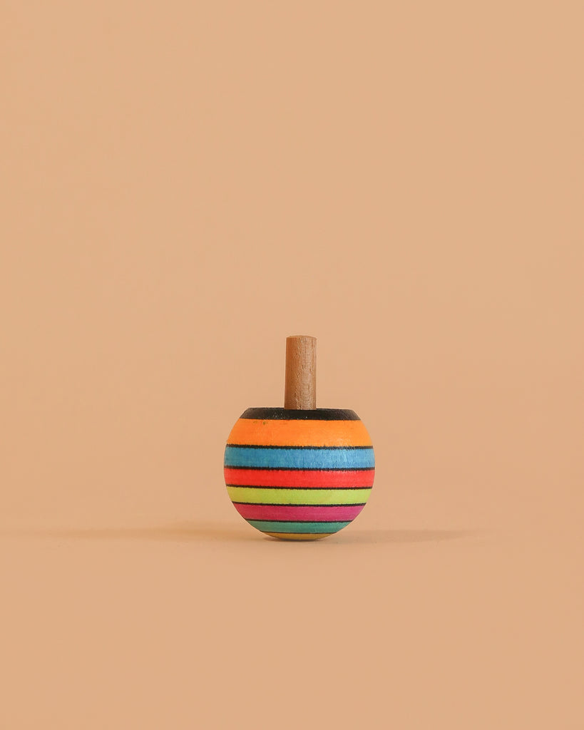 The Mader Turn-Over Top - Striped, made of maple wood with orange, blue, green, red, and black horizontal stripes, stands upright on a beige background.