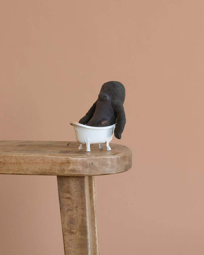 The Maileg Gorilla Bath Time Set features a small plush gorilla from the Mini Safari friends collection in a white bathtub, displayed on a wooden table against a beige background.